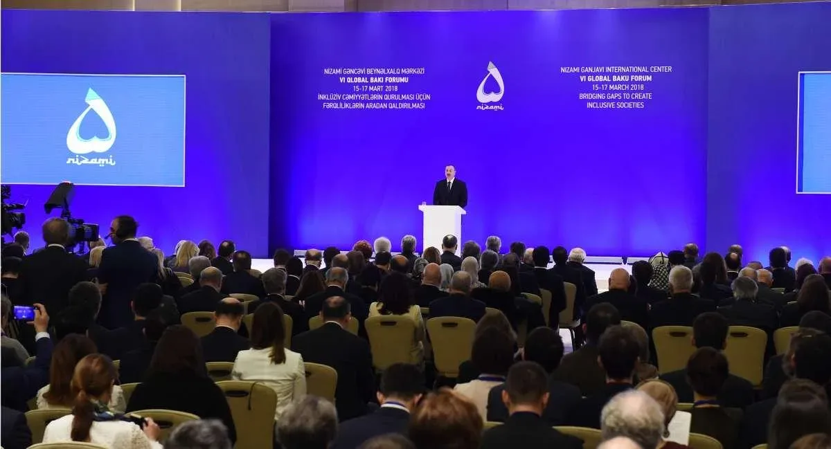 the forum hall — a speaker at the podium before a full audience