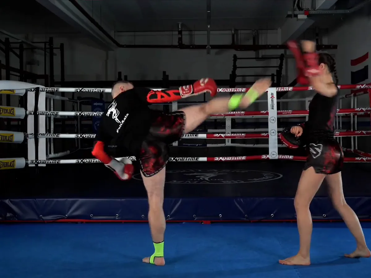 Kursdreh bei ExitAsia: ein Trainer tritt einen hohen Kick, eine Trainerin fängt ihn mit der Pratze ab, im Ring mit blauen Eckpolstern