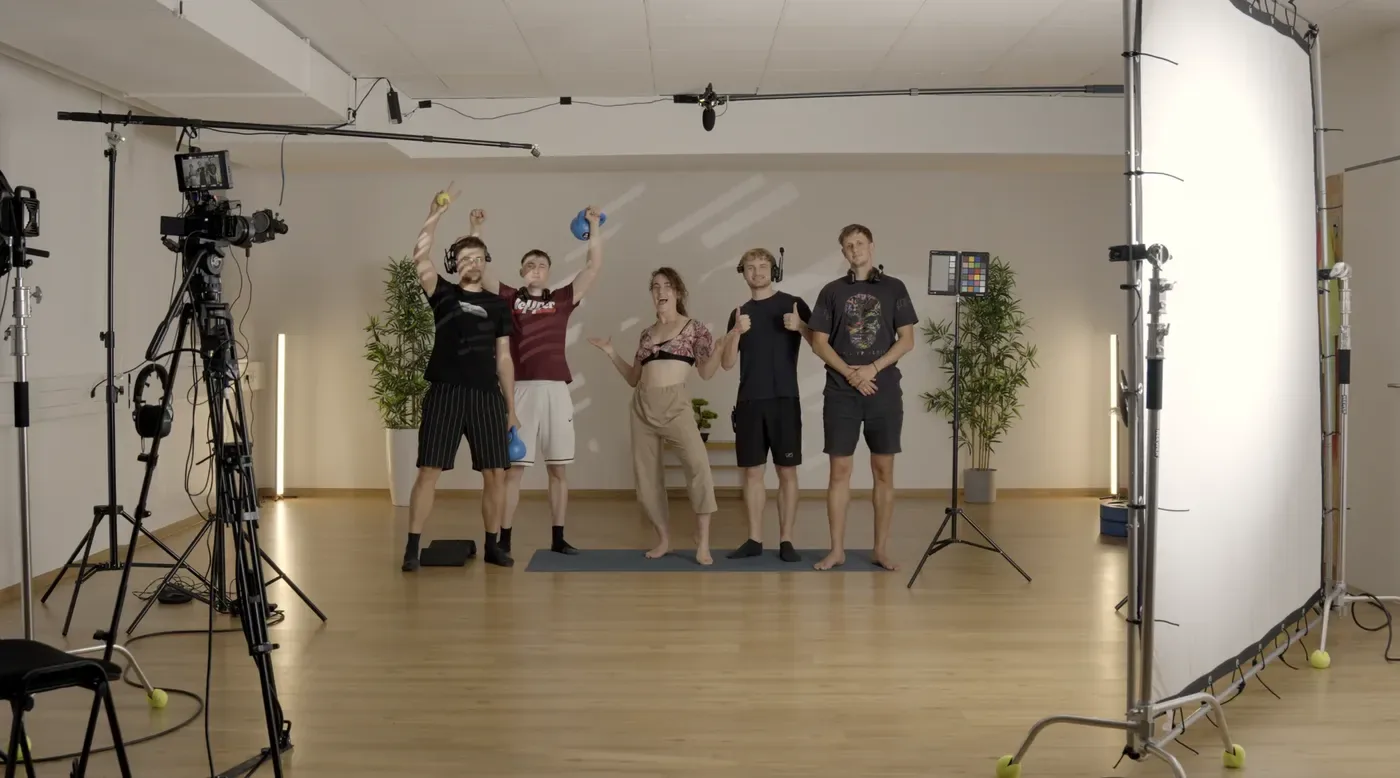 Drehtag im Studio: Elsa mit vier Leuten aus dem Team auf der Matte, links zwei Kameras auf Stativen, oben das Mikrofon an der Angel, rechts eine Farbkarte und eine weiße Reflektorwand