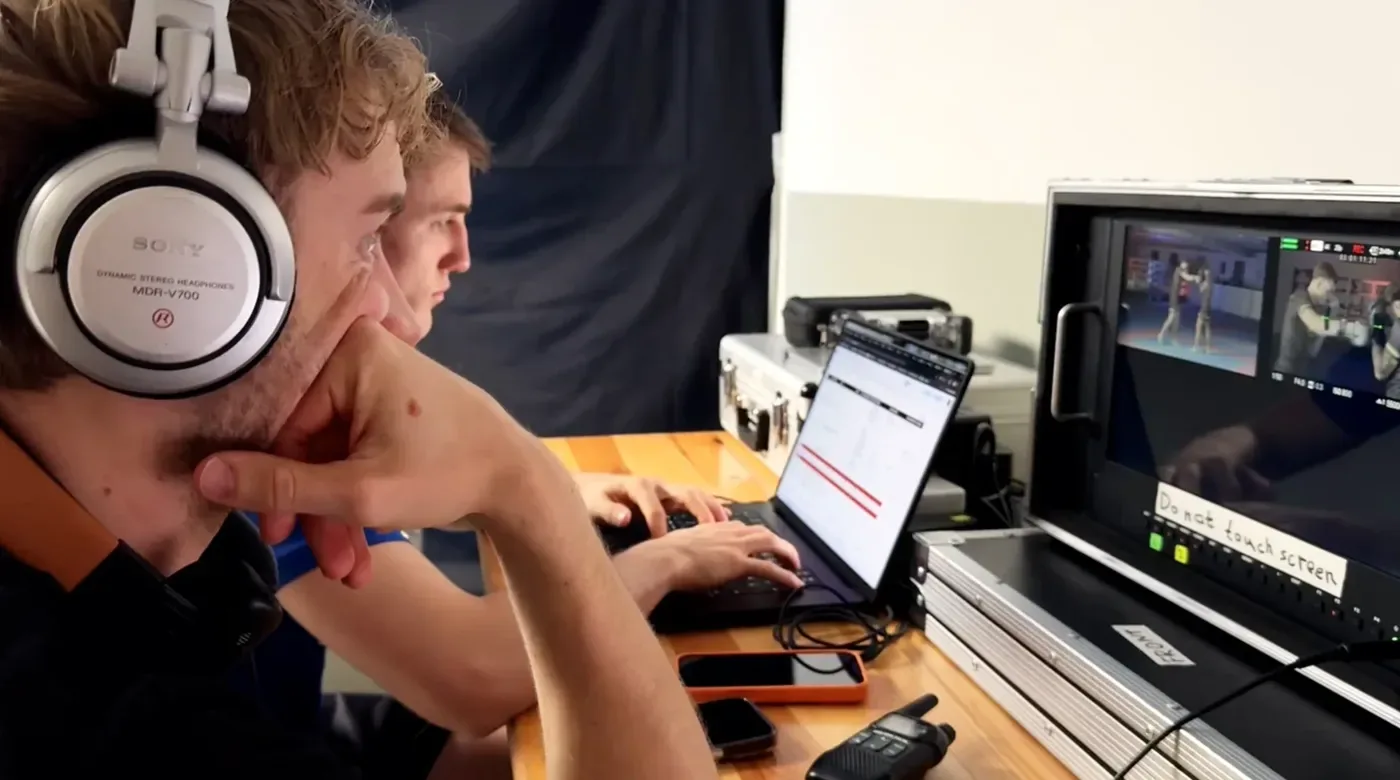 Regie am Set: zwei aus dem Team am Monitor, einer mit Kopfhörern, daneben ein Laptop mit dem Drehplan und ein Funkgerät