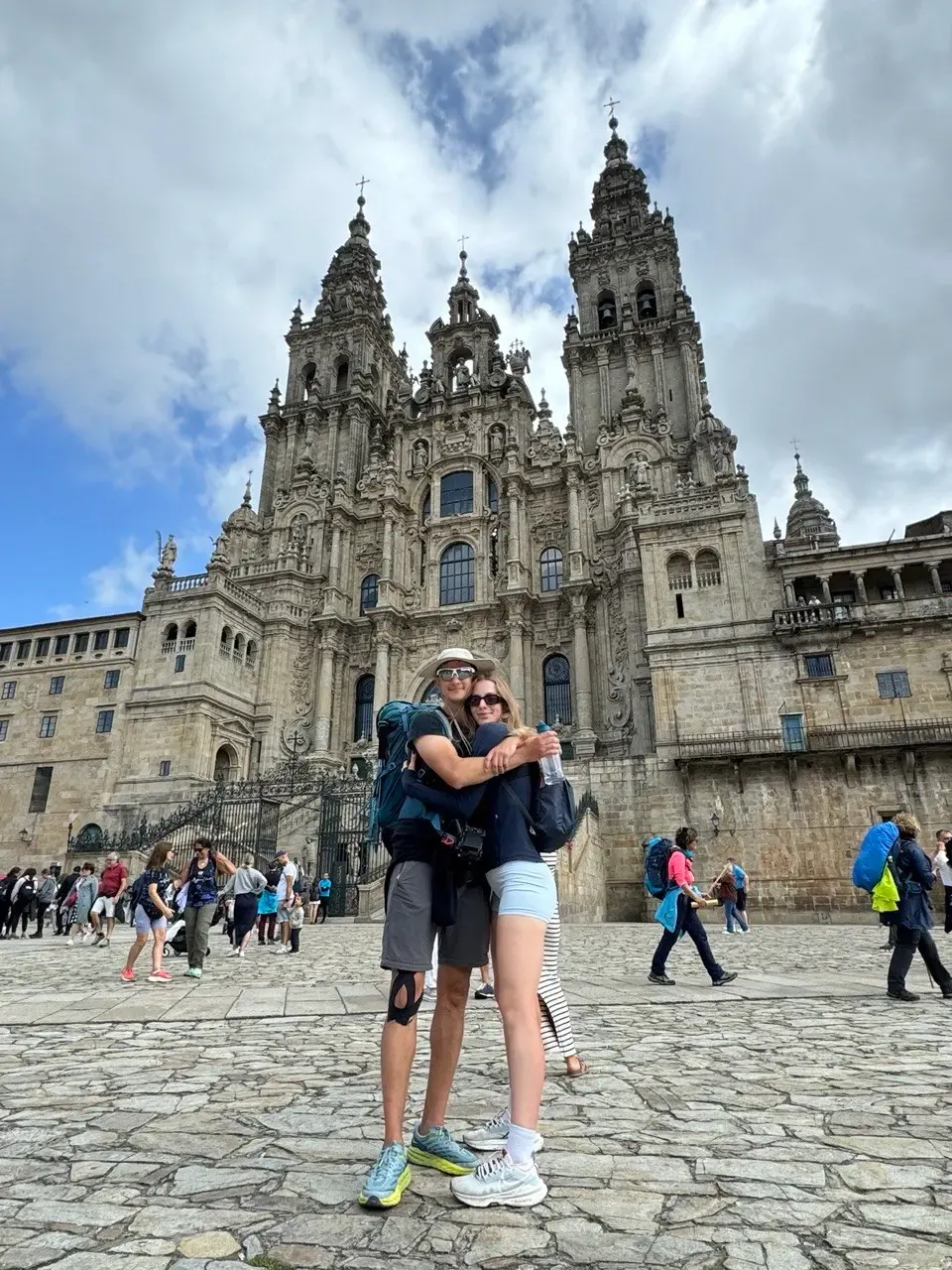 two pilgrims embracing in front of santiago de compostela cathedral, backpacks still on