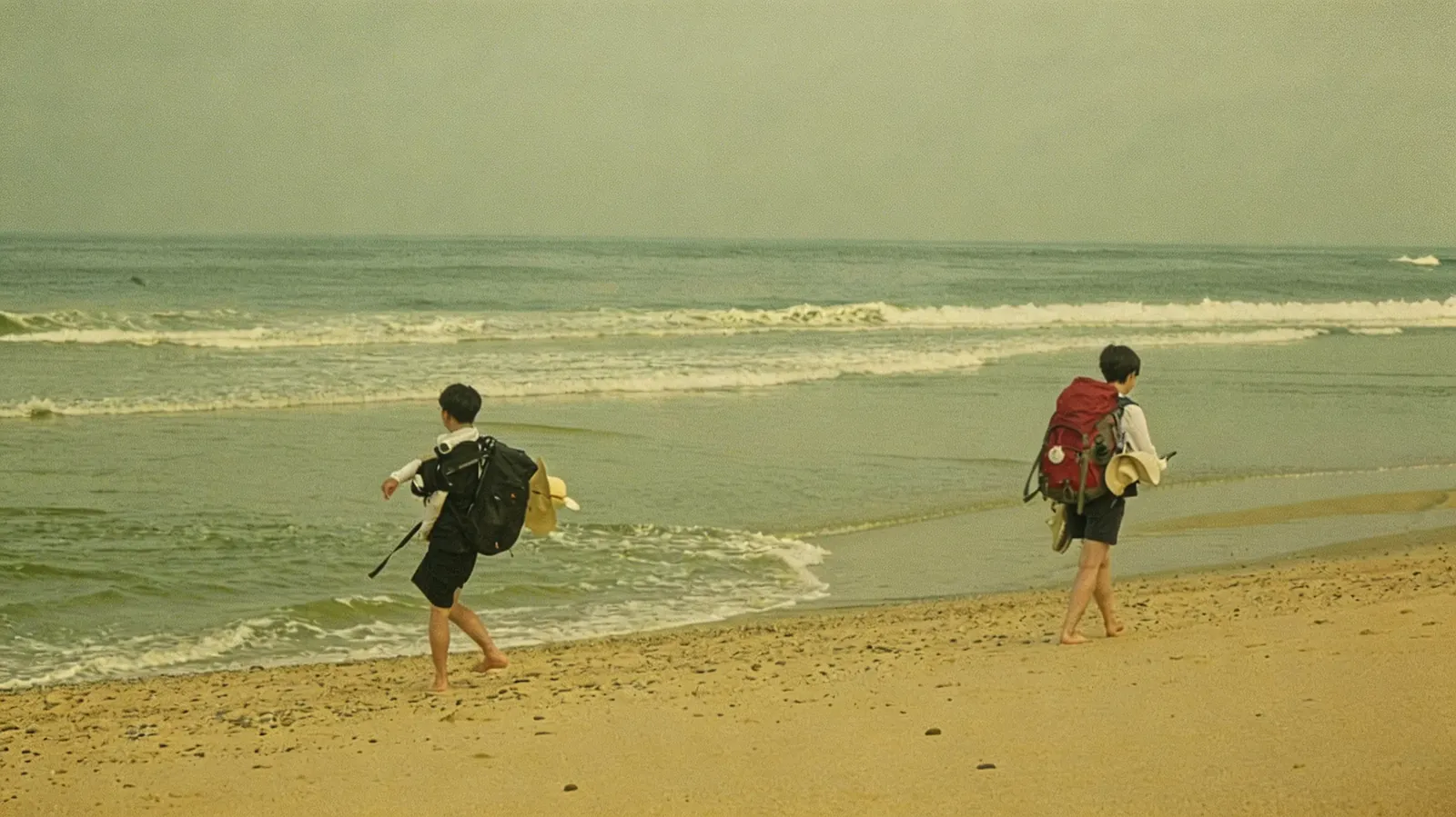 two pilgrims walking barefoot along a beach, boots in hand