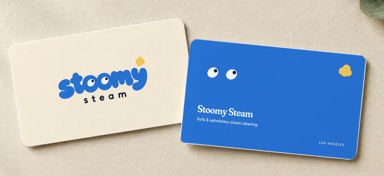 Two business cards: cream front with the Stoomy Steam logo, blue back with eyes — mockup