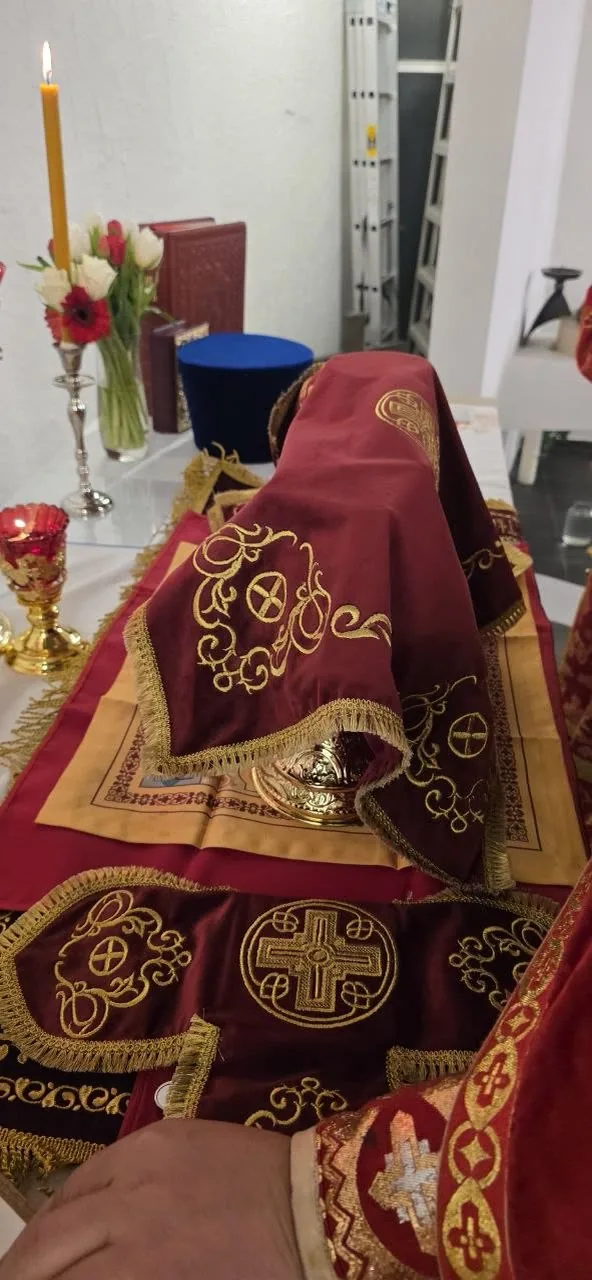 Der Altar vor dem Gottesdienst unter weinroten, goldbestickten Decken, daneben eine brennende Kerze und Blumen — eigenes Bild der Gemeinde