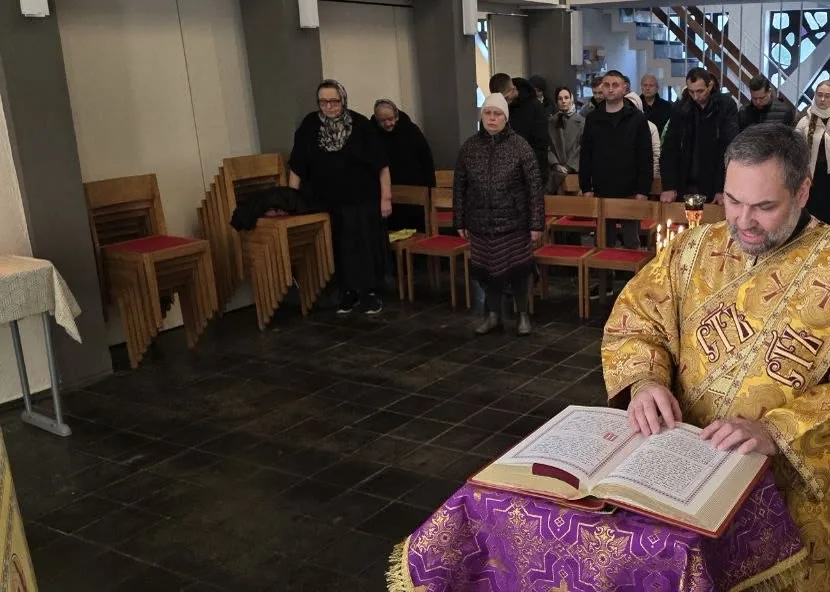 Ein Priester in goldenem Gewand liest das Evangelium vom Pult mit violettem Tuch, hinter ihm stehen erwachsene Gemeindemitglieder — eigenes Bild der Gemeinde